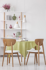 Vertical view of wooden chairs at round table with olive green tablecloth in bright elegant living...