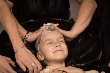 Smiling kid washing hair after haircut at hairdresser's.