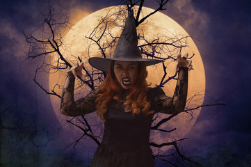 Scary halloween witch standing over dead tree, full moon and spooky cloudy sky
