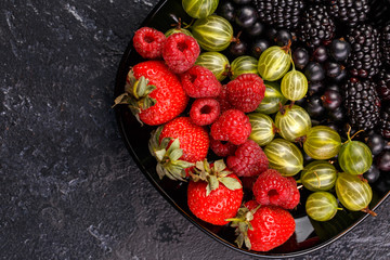 Image on top of blackberries, strawberries, raspberries, gooseberries on black plate