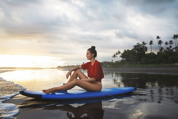 Woman sitting on surfboard on the beach after her surfing session