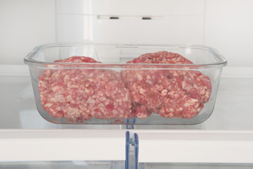 Minced raw meat in glass container is on shelf in open fridge. Ingredient for cooking meat dishes.