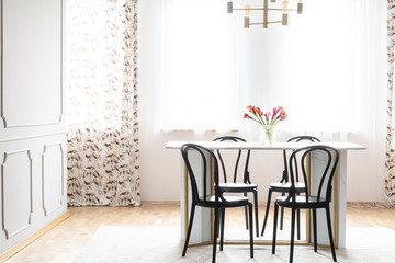 Natural light coming through windows into an elegant dining room interior with black wooden chairs around a marble table
