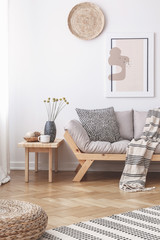 Wicker decorations and a painting on a white wall above a wooden sofa with cushions in a bright...