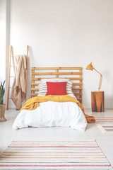 Red pillow and orange blanket on comfortable teenager bed with white bedding in elegant oldschool...