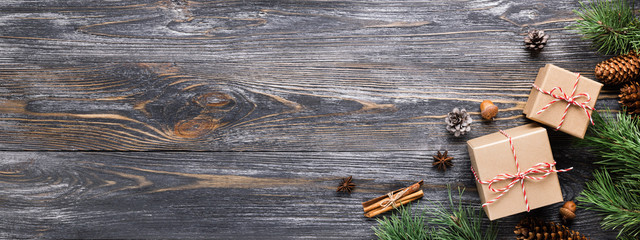 Christmas gifts in rustic stlye. Two gift boxes with cinnamon sticks, pine cones, anise stars and pine branches on wooden table. Top view, banner for website.