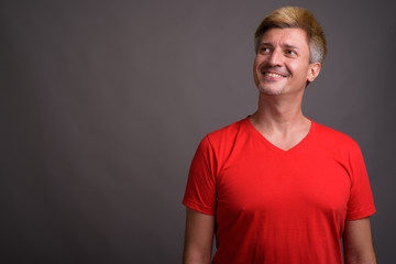 Man with blond hair wearing red shirt against gray background