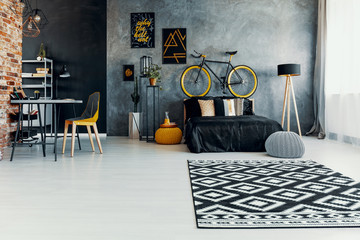 Patterned carpet and grey pouf in teenager's bedroom interior with posters and bicycle. Real photo