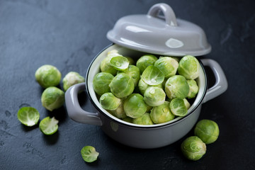 Raw fresh brussels sprouts in a pot, studio shot over black stone background