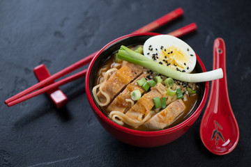 Bowl of ramen noodles with roasted chicken meat and egg, studio shot on a black stone background