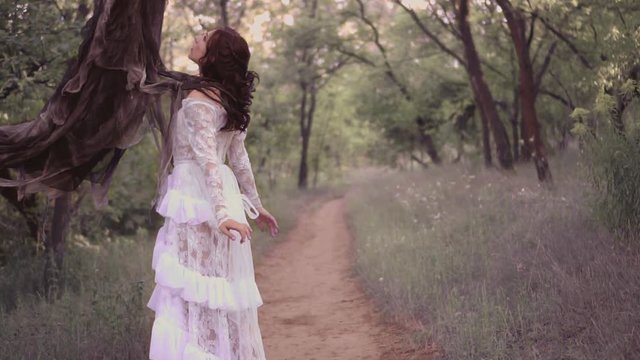 cute young girl in a white transparent long dress with a floral pattern and dark wavy hair was captured by the spirit of evil. death holds a woman with long claws by the shoulders, takes the soul