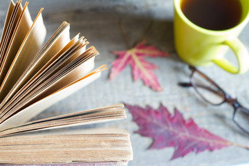 Open book autumn leaves tea and glasses abstract background on wooden boards
