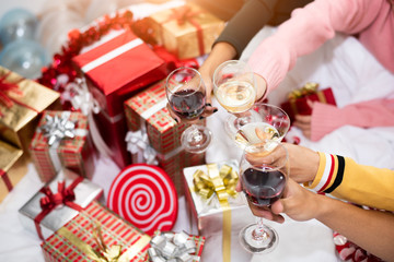 Hands of people celebrating New year party in home with wine drinking glasses and present background. New year and Christmas party concept. Happiness and Friendship and Funny together. Clinking glass