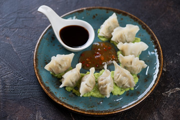 Boiled korean wontons with dipping sauces served on a turquoise plate over dark brown stone surface