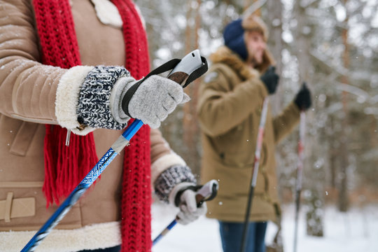 Side view portrait of active young couple enjoying skiing in beautiful winter forest, focus on unrecognizable woman holding ski poles, copy space
