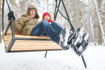 Full length low angle portrait of happy young couple sitting on wooden swing and laughing happily...