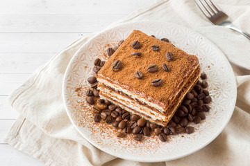 Delicious Tiramisu cake with coffee beans on a plate on a light background