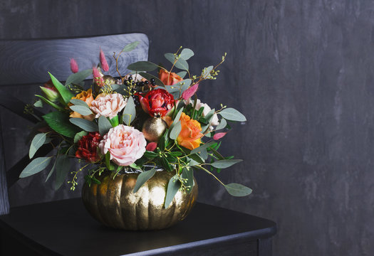Autumn floral bouquet in colored punpkin vase on black chair, copy space