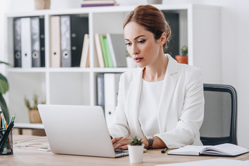serious professional businesswoman in formal wear working with laptop in office
