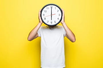 Foto op Canvas Young man holding big clock covering his face on yellow background © dianagrytsku