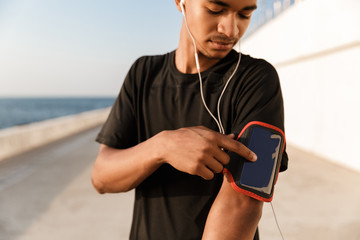Fototapeta premium Guy sportsman outdoors on the beach listening music with earphones using phone.