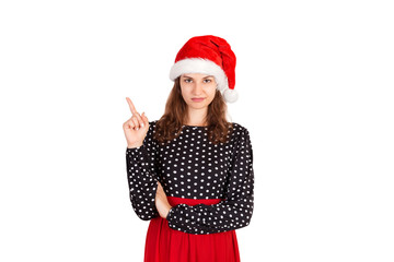 confused woman pointing finger up. emotional girl in santa claus christmas hat isolated on white background. holiday concept