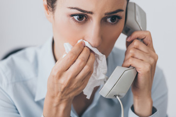 close-up portrait of sad businesswoman talking by wired phone with paper napkin at office