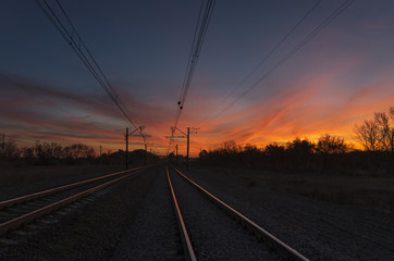 Sunset light reflects on the rails that running away to the horizon. Dark railway infrastructure at...