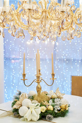 Christmas wreath and candlestick with candles under luxury chandelier on blurred, sparkling background, copy space. Winter holidays concept. Christmas background