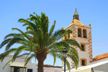 Fototapeta na wymiar Palm and the bell tower with blue sky in Fuerteventura, Spain. Tourism. catholic church Santa Maria de Betancuria in the Betancuria - small village and the old capital of Fuerteventura. 