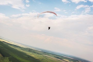 A white-orange paraglider flies over the mountainous terrain