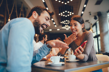 Young happy couple usinf smartphone in cafe