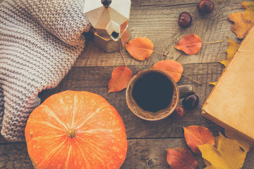Cup of coffee, cozy knitted scarf, autumn leaves, open book and pumpkin on wooden board. Autumn still life, vintage style. Flat lay.