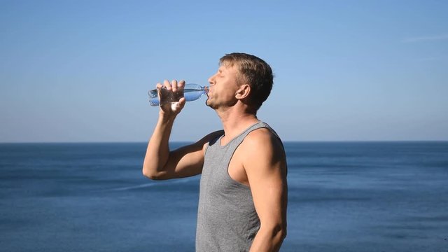 A man drinks water from a plastic bottle on the ocean, quenching thirst after exercise