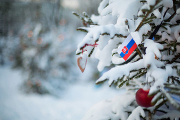Slovakia flag. Christmas background outdoor. Christmas tree covered with snow and decorations and Slovakian flag.  New Year / Christmas holiday greeting card.