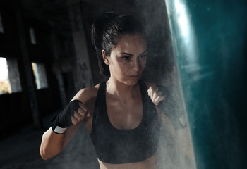 Fototapeta na wymiar Female boxer punching a boxing bag in warehouse.