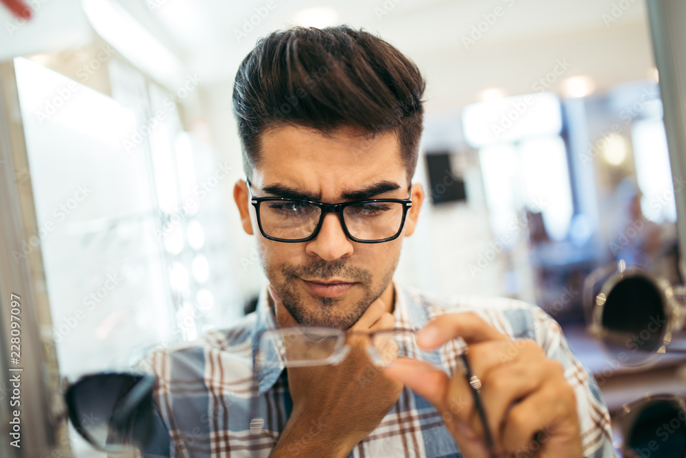 Poster handsome young man choosing eyeglasses frame in optical store.