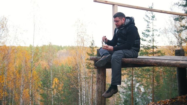 A man sits at a high altitude and eating the canned food with a knife
