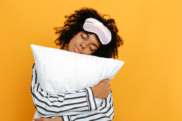 Sleeping. Dreams. Woman portrait. Afro American girl in pajama is hugging a pillow, on a yellow...