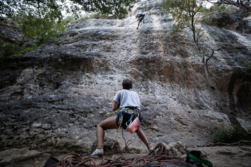 From below of anonymous man in harness looking up at mountain and checking partner climbing cliff