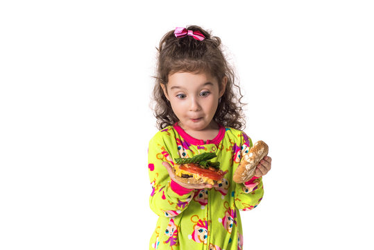 Girl in pajamas looks at a hamburger in surprise on a white background, isolated.