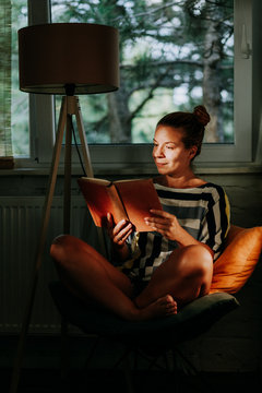 Young woman reading a book at home by the window