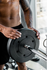 close-up partial view of muscular young sportsman putting weight plate on barbell in gym