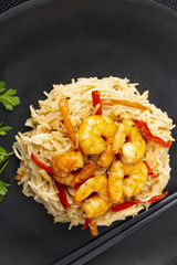 Fried prawns and rice noodles with spices on a black plate. Black background. Eastern food. Copy space. Vertical shot.