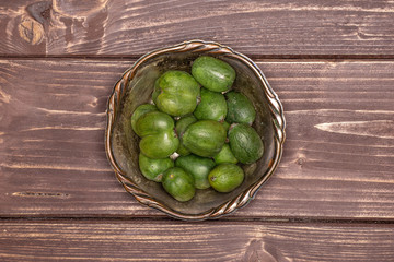 Lot of whole fresh green mini baby kiwi fruit in old iron bowl flatlay on brown wood