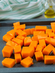 Chopped pumpkin being drizzled with olive oil before baking on a tin
