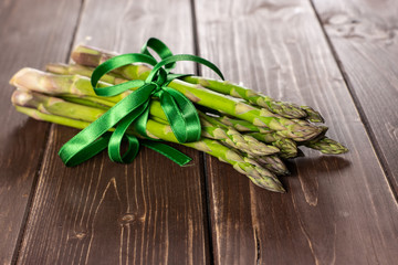 Bundle of lot of whole fresh green asparagus spear tied by green ribbon on brown wood
