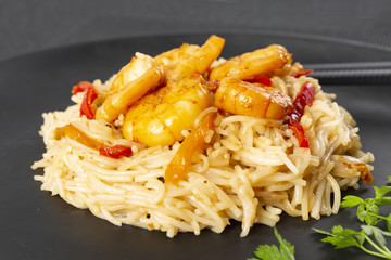 Fried prawns and rice noodles with spices on a black plate. Black background. Eastern food. Copy space.