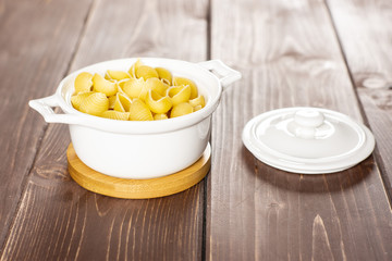 Lot of whole raw yellow pasta conchiglie variety in a ceramic stewpan on brown wood
