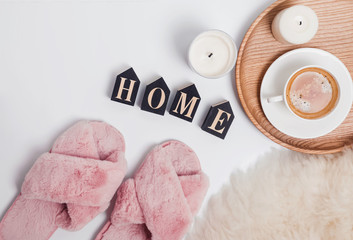 Pink fluffy feminine slippers, coffee and wooden letters arranged in a word Home